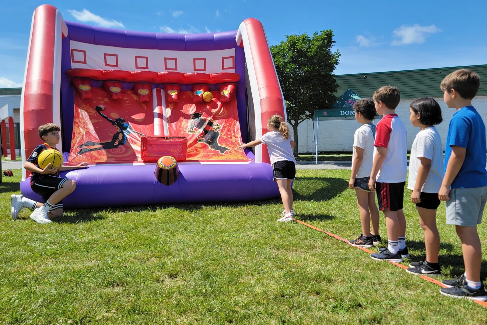 Your real inflatable basketball game with a line of kids waiting to play (edited from your photo with Seedream — keeps the actual game).